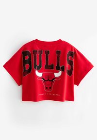 Crveni skraćeni majica s boldnim crnim slovima koja pišu "BULLS" i grafikom glave bika na leđima, s okruglim izrezom i kratkim rukavima.