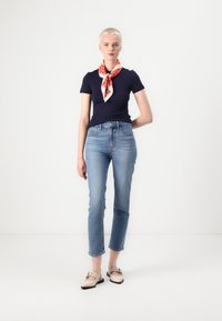 Jūros mėlynumo lieknas t-shirt, šviesiai mėlynos tiesios kojelės džinsai ir smėlio spalvos avalynė su dekoratyvine kaspina. Raudonos ir baltos spalvų juostuota skara ant kaklo.