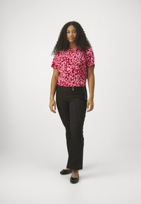Short-sleeve, patterned top in red and white, paired with black fitted pants featuring front zip and button detail. Flat black shoes complete the look.
