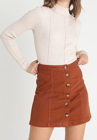 Ljust beige ribbad långärmad topp i kombination med en rostfärgad jeanskjol med sex knappar framtill.