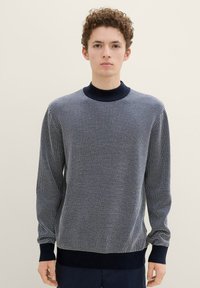 Marineblauwe en witte horizontaal gestreepte gebreide trui met een hoge kraag en geribde manchetten en zoom. Zachte textuur, comfortabele pasvorm.