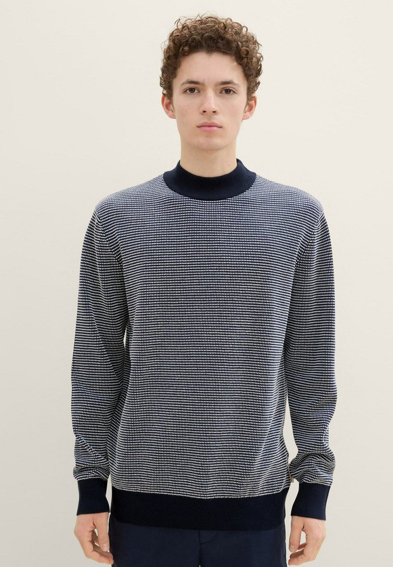 Marineblauwe en witte horizontaal gestreepte gebreide trui met een hoge kraag en geribde manchetten en zoom. Zachte textuur, comfortabele pasvorm.