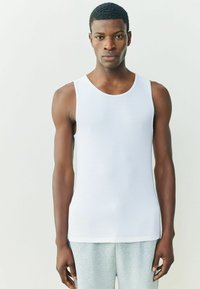 Biele rebrované tielko s okrúhlym výstrihom, s priliehavým strihom a hladkou textúrou, skombinované so svetlosivými teplákmi.