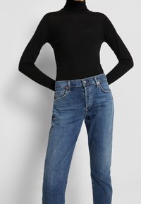 Svart polotröja matchad med blå denimjeans. Jeansen har en klassisk femficksdesign med ljusblekningar och kopparbeslag.