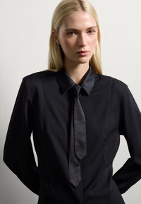 Black silk shirt with a pointed collar and a matching tie. Features a smooth texture and structured design, emphasizing clean lines.