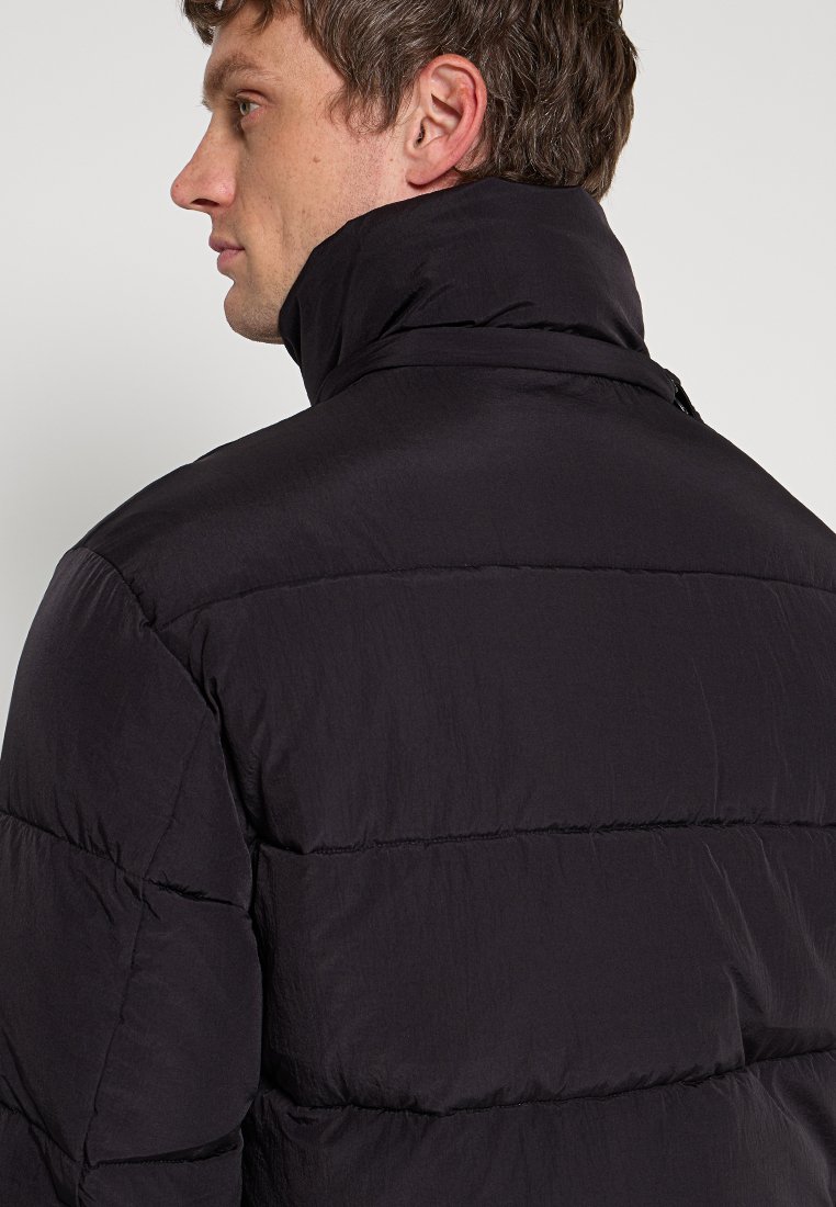 Giubbotto imbottito nero con colletto alto, caratterizzato da un design trapuntato e una texture liscia. La vista posteriore mostra cuciture orizzontali e materiale leggero.