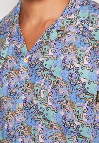 Korte mouw shirt in lichtblauw, lila en perzik met abstracte geometrische patronen; heeft een kraag en knopen in een natuurlijke afwerking.
