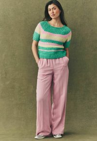 Kortærmet strikket sweater med grønne, gule og pink striber; parret med afslappede pink bukser og sølvfarvede sneakers.