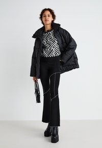 Doudoune noire sur un pull à motifs noir et blanc, associée à un pantalon évasé noir avec des coutures blanches et des bottes à plateforme.
