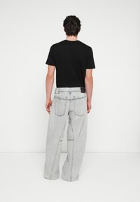 Fekete rövid ujjú póló világosszürke, széles szárú farmerral párosítva, mely két hátsó zsebbel és kontrasztos varrásokkal van ellátva a varratok mentén.