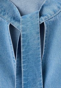 Top de denim azul claro con diseño de ojo de cerradura en la parte trasera y detalle de lazo. Textura suave con acentos de costuras limpias.