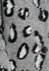Grijze jas van een zachte, gestructureerde stof met zwart-witte luipaardprint; inclusief een glanzende zwarte knoop detail.