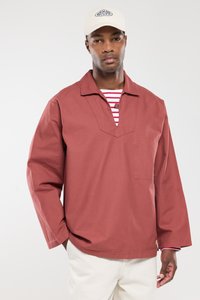 Rustkleurig, lang mouw shirt met een V-hals en een voorzak. Daaronder is een horizontaal gestreept shirt zichtbaar. Het model draagt een beige pet.