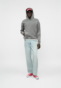 Γκρι φούτερ με μπροστινή τσέπη, συνδυασμένο με ανοιχτό μπλε τζιν και κόκκινες Converse sneakers. Το φούτερ διαθέτει ρύθμιση με κορδόνια στην κουκούλα.