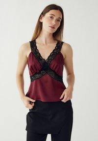 Bourgogne satin cami med en dyb V-udskæring og sort blondekant og akcenter, samt en afslappet pasform og justerbare stropper.
