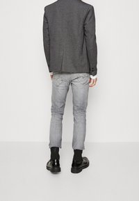 Szara dopasowana marynarka o fakturowanym wykończeniu, zestawiona z jasnoszarymi dżinsami. Czarny obuwie dopełnia strój. Widoczne guziki na marynarce.