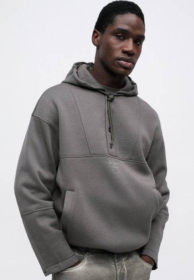 Hanorac gri cu un finisaj texturat, dotat cu o glugă reglabilă, buzunar frontal și un logo brodat pe piept.