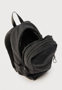 Sac à dos noir avec deux compartiments zippés partiellement ouverts, bretelles rembourrées et une poignée de transport supérieure sur un fond clair.