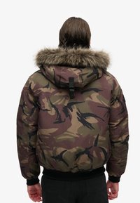 Kamufleret pufferjakke med en faux pelsforet hætte, sorte accenter, elastiske manchetter og en afslappet pasform. Har en tykk, polstret design.
