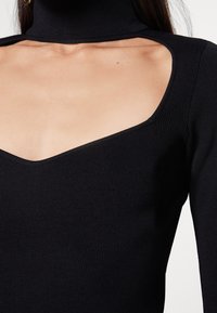 Svart ribbad tröja med hög hals, djup V-ringning och öppna axeldetaljer, med en jämn textur och slim-fit design.