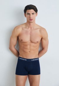 Marineblaue Boxer-Briefs mit einem weichen elastischen Bund, der das Lacoste-Logo trägt. Glatter Stoff, figurnahe Passform und mittellange Beine.