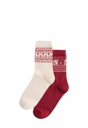 Zwei Socken: Eine cremefarbene mit roten geometrischen Mustern am Bund, die andere rot mit weißen Motiven von Häusern und Bäumen nahe der Spitze. Mischgewebe aus Baumwolle.
