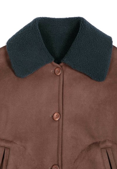 Manteau marron avec grand col en peau retournée noir et trois boutons marron sur le devant, montrant le haut de la poitrine et la zone du col.