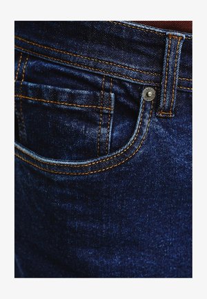 Ciemnoniebieskie dżinsy z kontrastowymi pomarańczowymi szwami, z przednią kieszenią i metalowym zapięciem. Faktura wydaje się gładka.