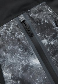 Gros plan d'un panneau en tissu marbré noir et gris avec une fermeture éclair imperméable dotée d'une languette noire mate.