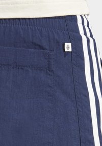 Navy blue athletic shorts made of textured fabric, featuring a pocket and white stripes along the side. A small globe logo is visible.