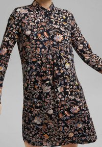 Blommig klänning i svart tyg med långa ärmar, krage och samlad midja. Mönster inkluderar färgglada blommor och lövverk.