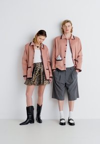 Dve modelky nosia koordinované oblečenie. Ružová bunda s čiernymi detailmi, skombinovaná s sukňou v leopardom vzore a šedými šortkami. Čierne čižmy a topánky dotvárajú vzhľad.