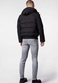 Czarna puchowa kurtka z kapturem, z pikowanym wzorem i ściągaczem u dołu. Noszona z szarymi dopasowanymi dżinsami i czarnymi butami.