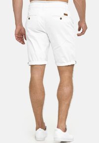 Witte katoenen shorts met opgerolde zoom, twee achterzakken met knopen en een beige lederen label op de rechter achterrand van de tailleband. Witte sneakers gedragen.
