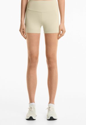 Lichtgroene, strakke sportshorts met een hoge taille, korte pijpen en een gladde textuur, gecombineerd met lichte sneakers en witte sokken.