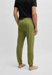 Groene katoenen joggingbroeken met een elastische taille en taps toelopende pijpen. Voorzien van zijzakken en een gladde textuur. Gekoord met een zwarte shirt.
