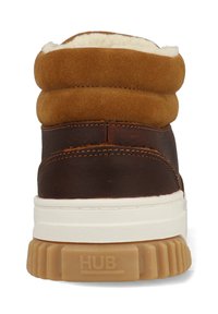 Bruine leren en suède enkelboot met een crèmekleurige bontvoering, witte middenzool en een gestructureerde rubberen outsole met de merknaam "HUB."