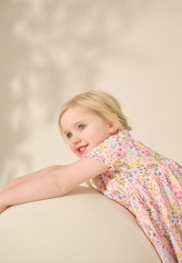 Robe à motifs floraux avec manches courtes, présentant des fleurs roses, jaunes et violettes. Tissu léger aux tons pastels qui tombe doucement.