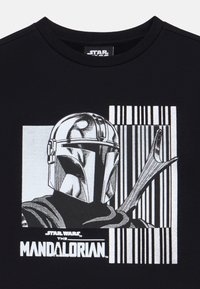 T-shirt nera con una grafica di una figura con elmo da "The Mandalorian", con colori monocromatici e elementi di sfondo a strisce.