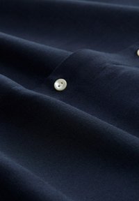 Námořnická látka s hladkým povrchem, zdobená bílým knoflíkem. Materiál se zdá být lehký a je složen, aby ukázal hloubku.
