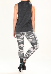 Top atletico grigio senza maniche con scollatura rotonda, abbinato a leggings aderenti grigi in stile camouflage. Le scarpe includono sneakers nere con accenti turchesi.