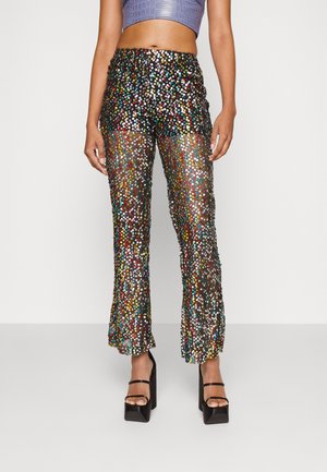 Modelen har højtaljede gennemsigtige sorte bukser dækket af flerfarvede palietter, kombineret med sorte plateau-sandaler og en cropped lilla top.