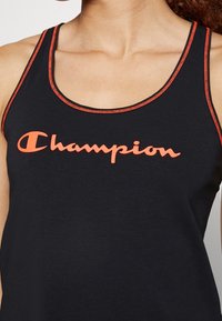 Svart linne med orange sömmar, med en framträdande orange "Champion"-logotyp över bröstet. Lättviktsmaterial och ärmlös design.