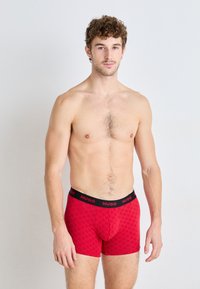 Red boxer briefs made of stretch fabric, featuring a checker pattern, black elastic waistband with "HUGO" logo, and a fitted design.