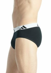 Zwarte herenslips met een witte elastische tailleband met zwarte strepen. Gemaakt van een gladde stof, hebben ze een strakke pasvorm en minimale bedekking.