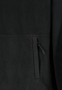 Schwarzer Fleece-Stoff mit einer vertikalen Reißverschlusstasche, die auf der rechten Seite einen kleinen Zugtab hat.