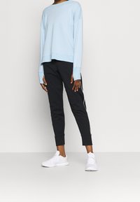 Ljusblå långärmad skjorta, avslappnad passform, tillsammans med svarta joggarbyxor med vita sidostråk och vita sportskor.