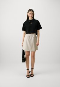 Svart kortermet t-skjorte, beige omslagsskjørt, svarte stilettosandaler og en blank svart håndveske. Minimalistisk design totalt sett.