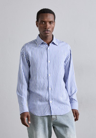 Chemise rayée bleu et blanche avec des boutons, manches longues, col et coupe décontractée, associée à un jean bleu clair. Texture de tissu douce.