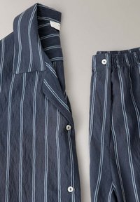 Haut et bas de pyjama bleu foncé avec des rayures blanches verticales et des boutons blancs sur un fond clair.